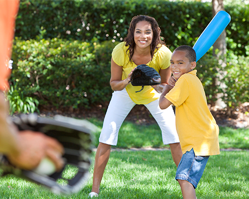 young boy playing baseball with his mom and dad in the yard